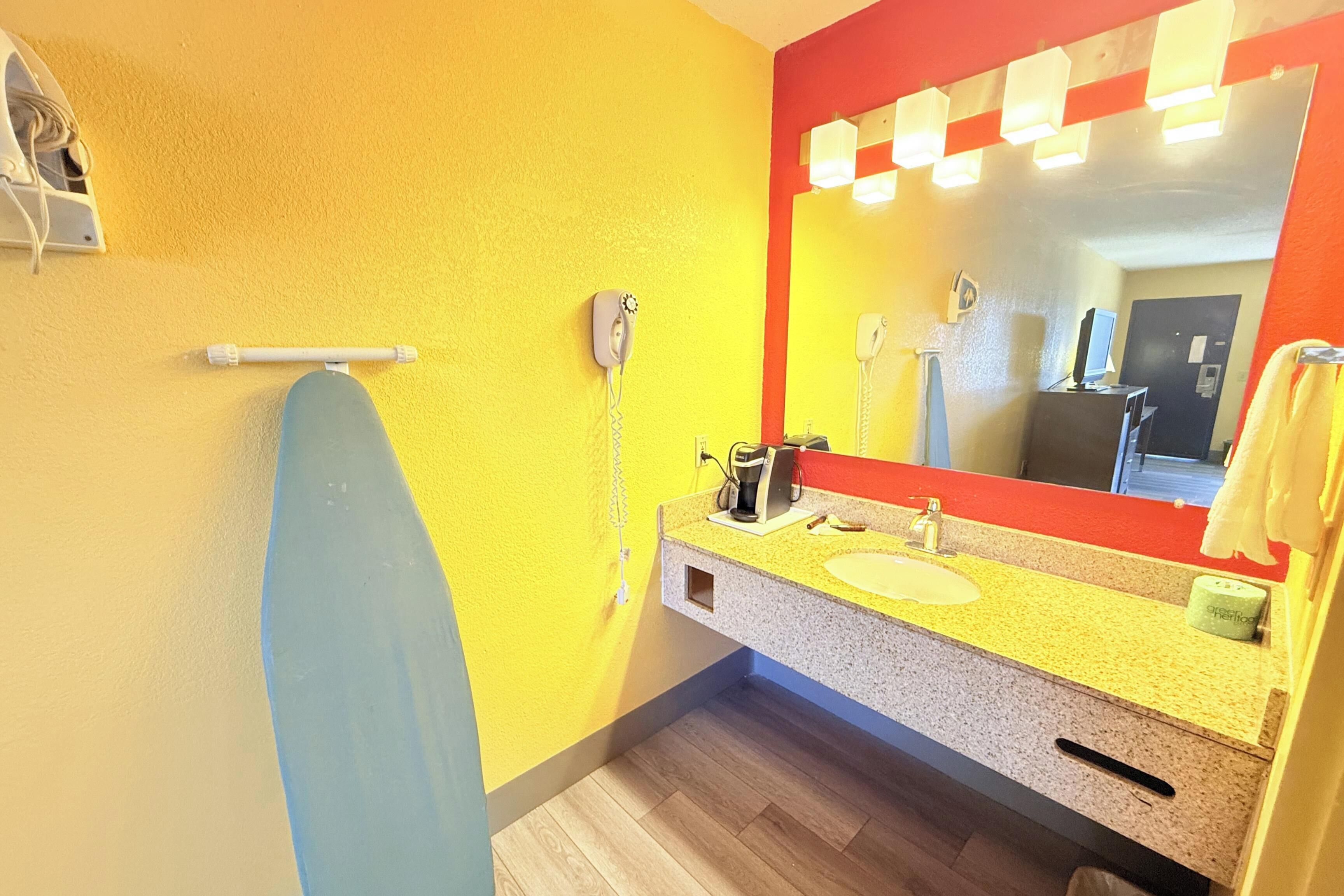 A bathroom with a yellow wall, a blue towel rack, a sink with a mirror, and a telephone.