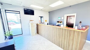 A reception area with a wooden reception desk, a flat-screen TV mounted on the wall, a potted plant, and a door with a decorative handle. - OYO Hotel Williamston (Williamston)