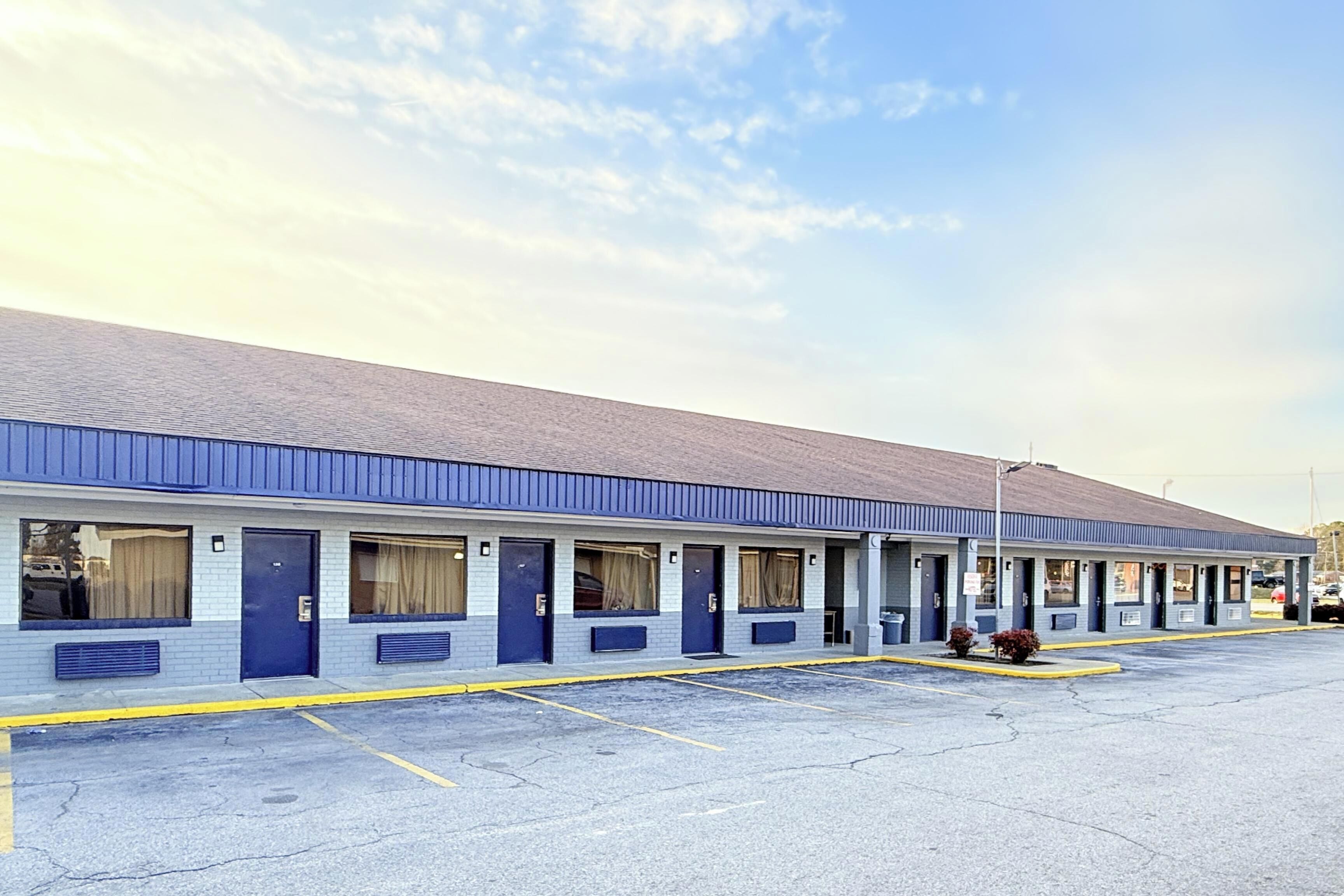 A motel with a row of rooms, a parking lot, and a clear sky.