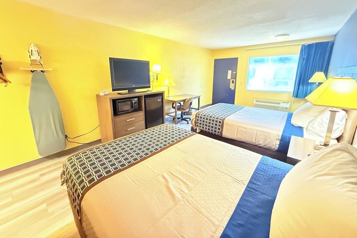 A hotel room with two beds, a desk, a television, and a window with curtains.