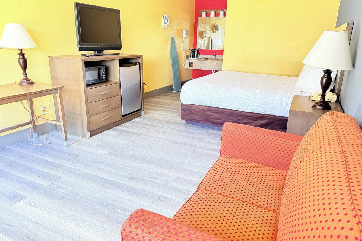 A hotel room with a bed, a desk with a television, a microwave, and a small refrigerator.