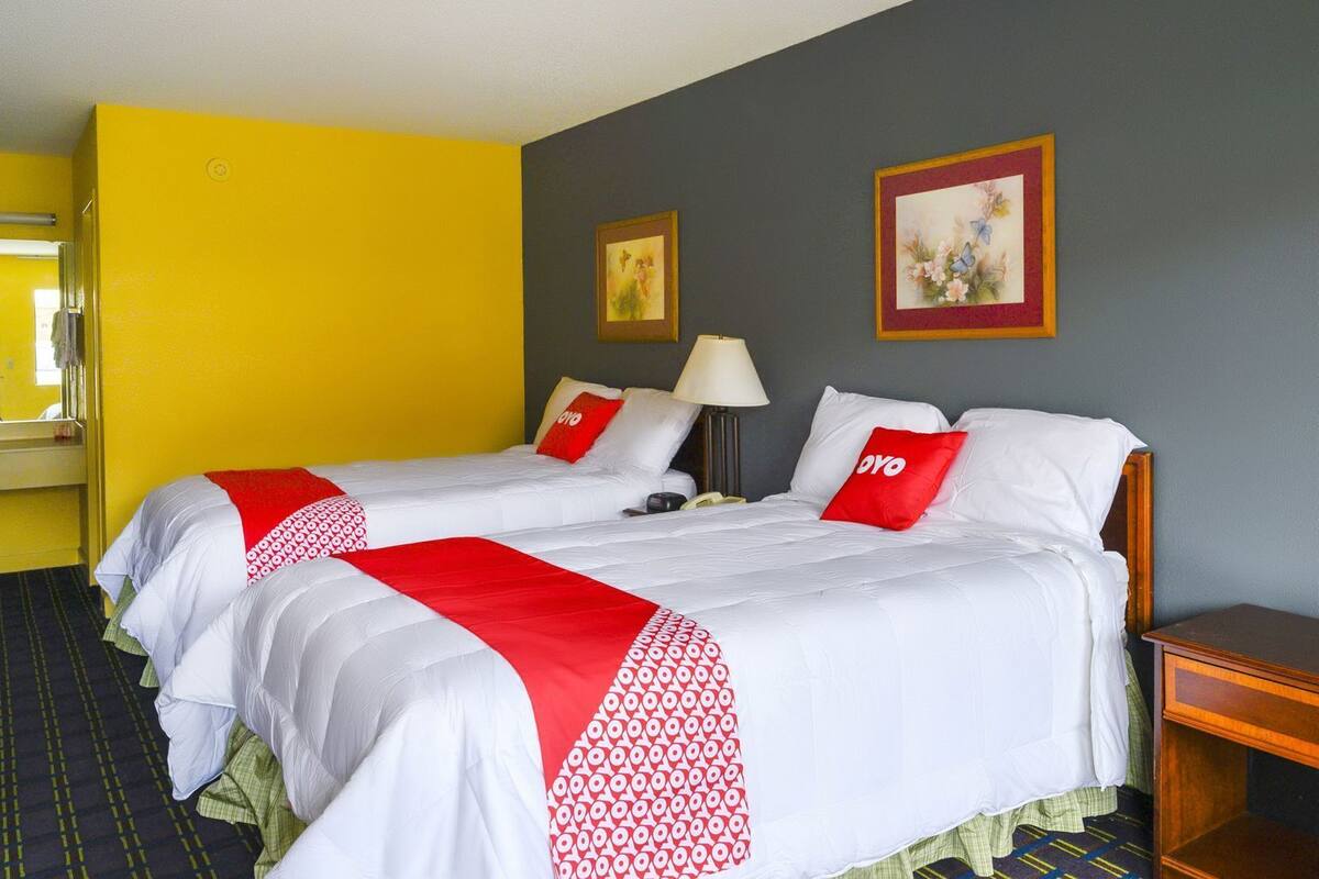 A hotel room with two beds, a nightstand, a lamp, and two framed pictures on the wall.