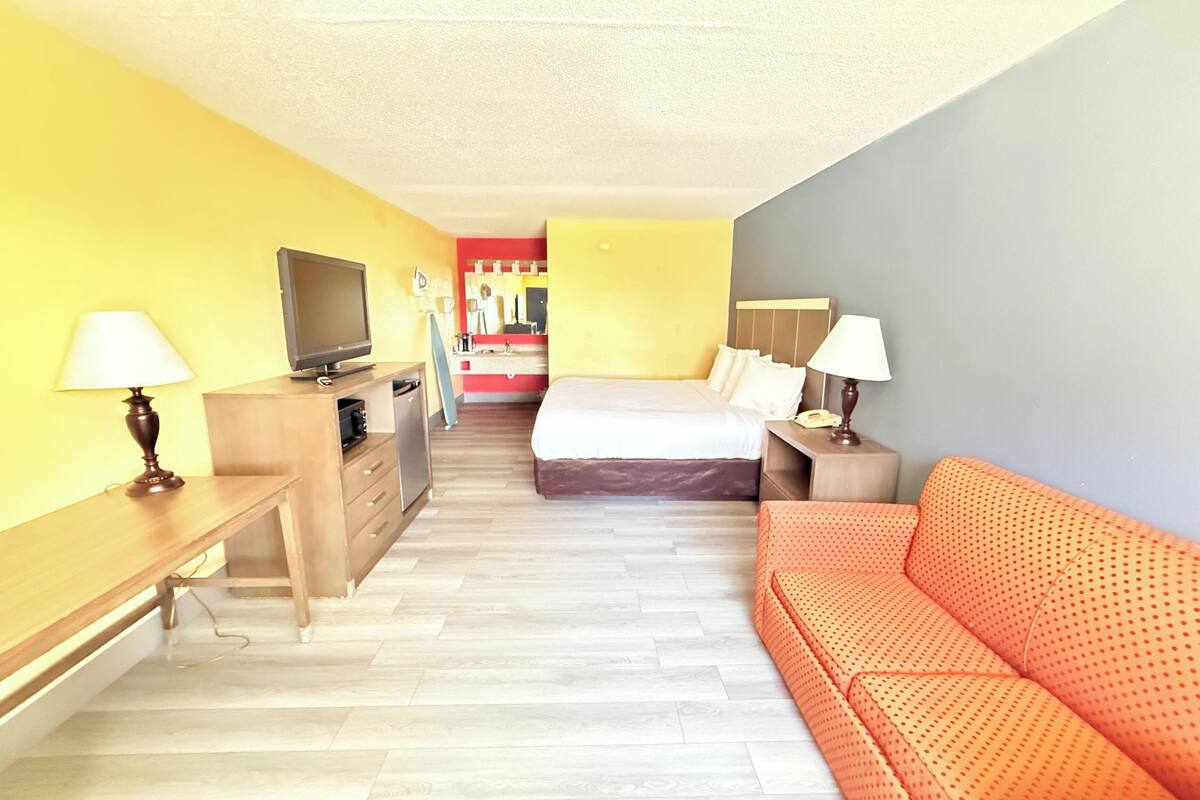 A hotel room with a bed, a sofa, a TV, a desk, and a mirror.