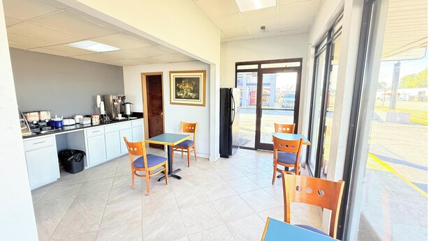 A restaurant with a kitchen area, dining tables, chairs, and a large window with a view of the outside. - OYO Hotel Williamston (Williamston)
