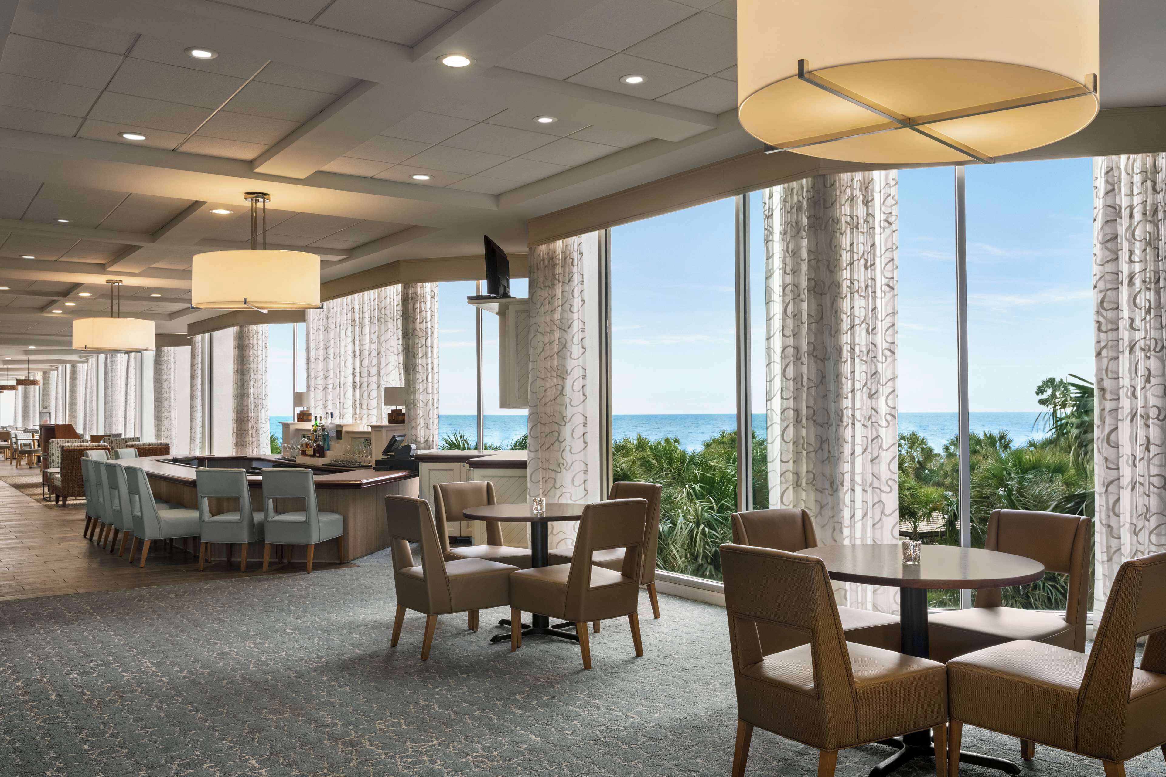 A spacious hotel lobby with a large dining area, a bar, and a view of the ocean.