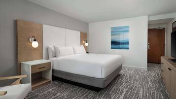 A modern hotel room with a large bed, bedside tables, a TV, and a painting on the wall.
