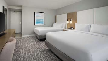 A hotel room with two beds, a desk, a TV, and a framed picture on the wall.