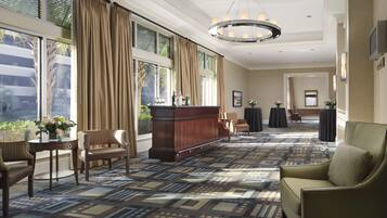A spacious hotel lobby with a patterned carpet, a reception desk, and seating areas.