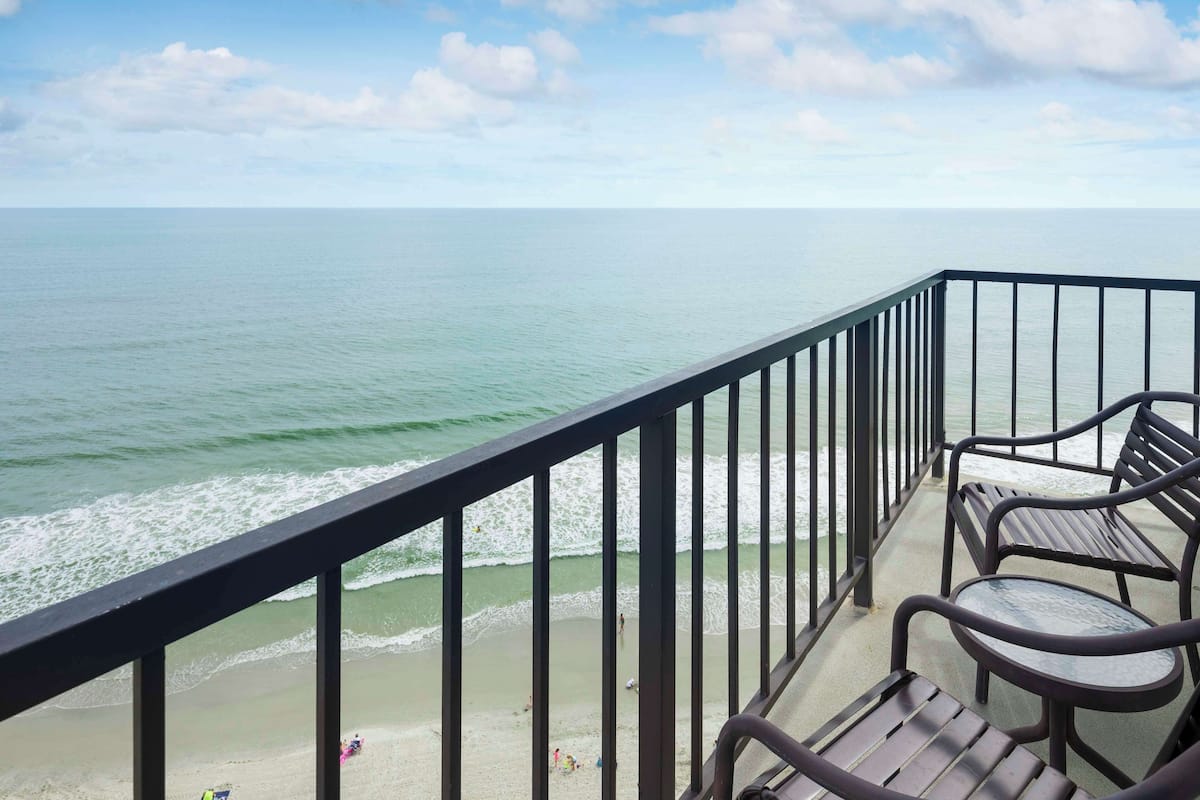 A balcony with a view of the ocean, equipped with metal chairs and a glass table.