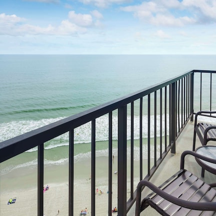 A balcony with a view of the ocean, equipped with metal chairs and a glass table.