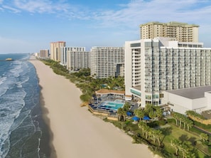 A beachfront hotel with multiple high-rise buildings, a sandy beach, and a pool area.