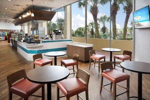 Enjoy meals in a stylish restaurant with round tables, a central counter, and a seating area offering views of palm trees and the beach.