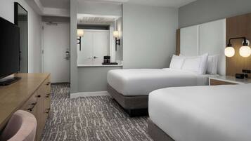 Une chambre d’hôtel avec deux lits, un bureau avec une télévision, une salle de bain avec un miroir et une moquette à motifs.