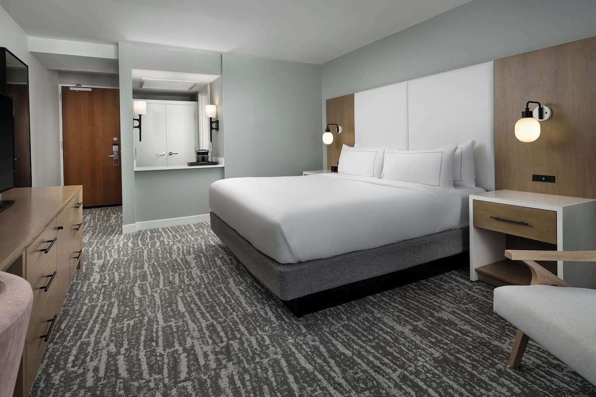 A modern hotel room with a large bed, bedside tables, a desk, and a wardrobe.
