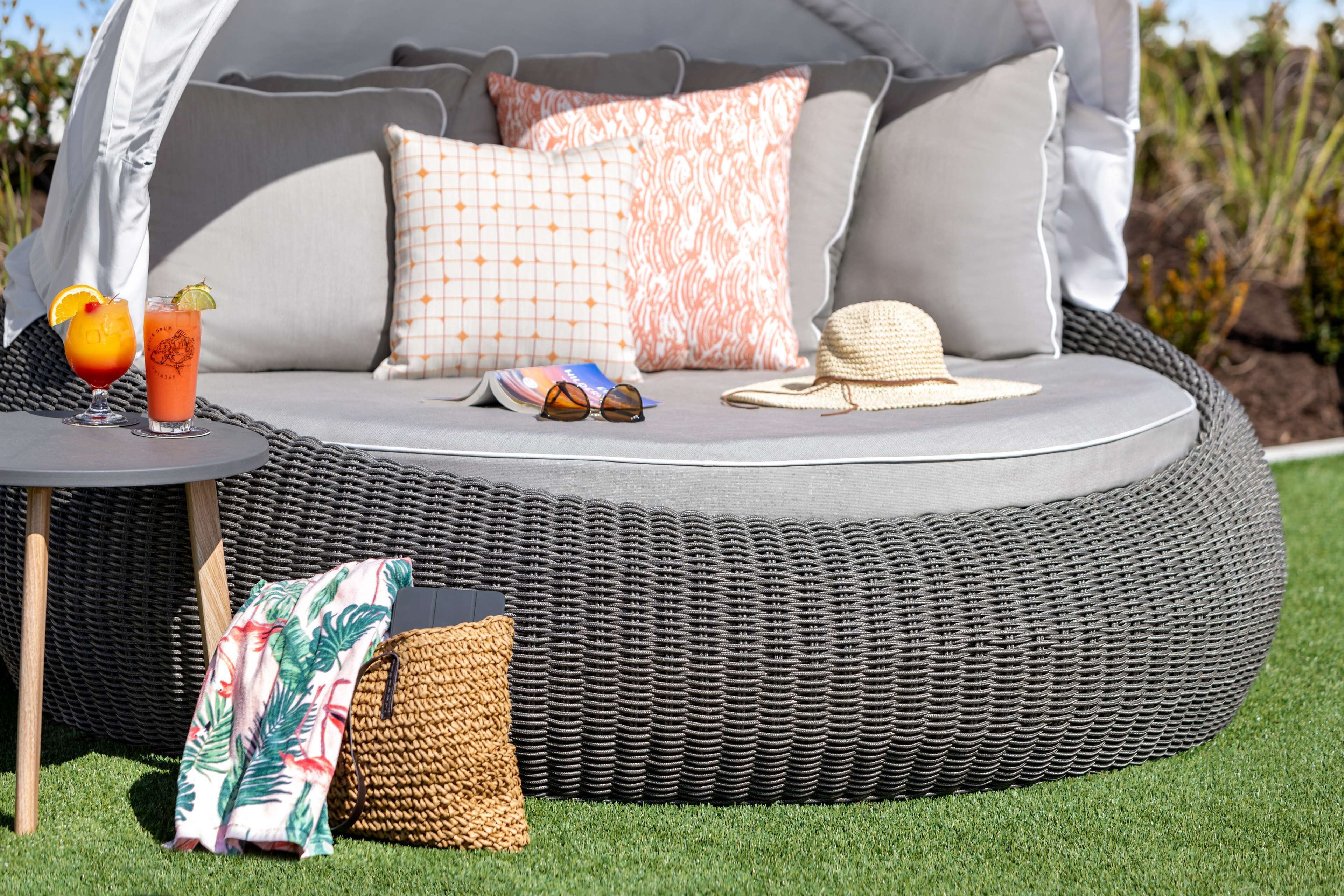 A round outdoor seating area with a wicker sofa, a small table with drinks, and a hat.
