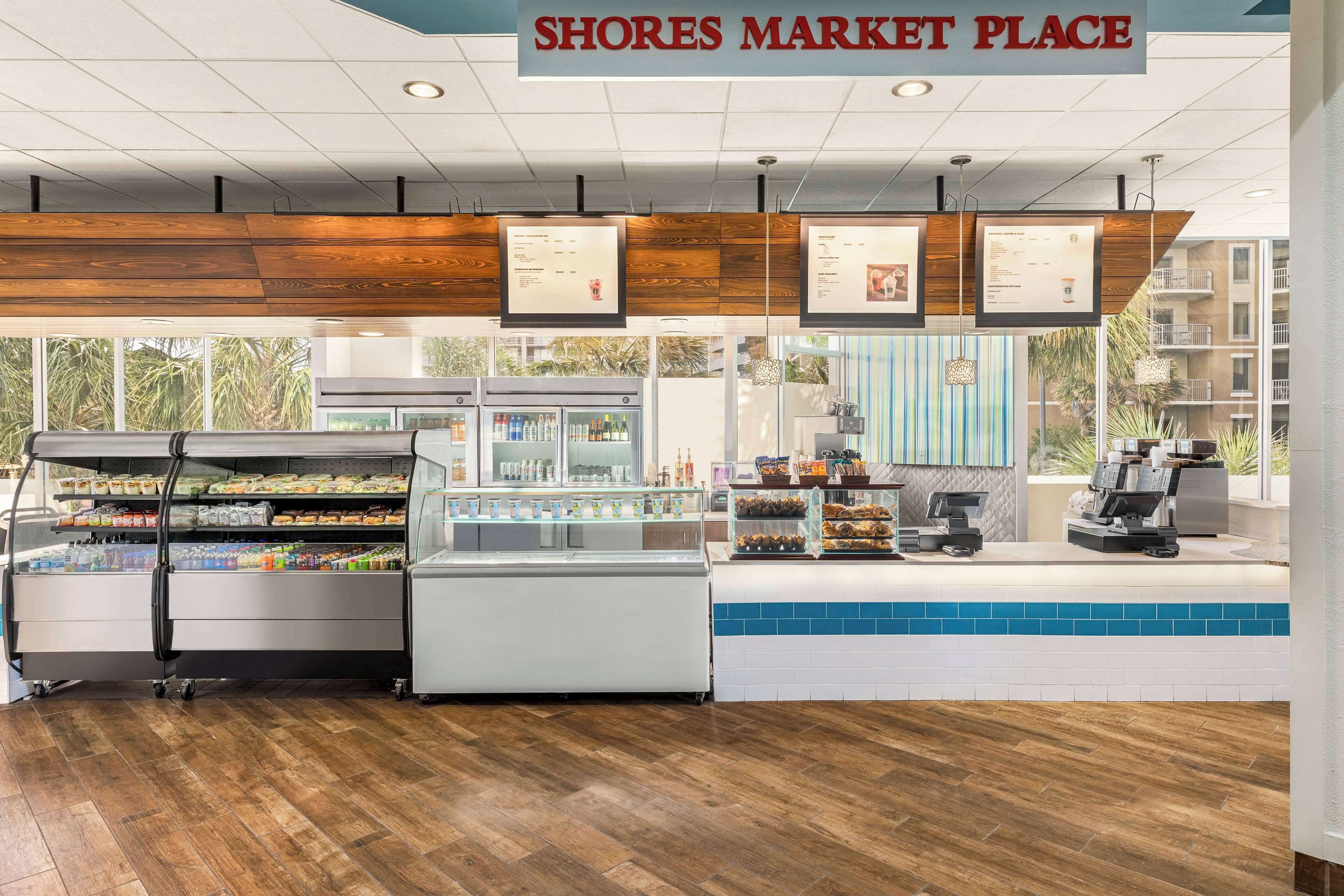 Un espace de restauration avec une enseigne indiquant « SHORES MARKET PLACE », proposant une variété de stands de nourriture et un distributeur de café.