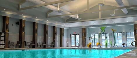 An indoor swimming pool with clear water, surrounded by lounge chairs and a modern ceiling design.