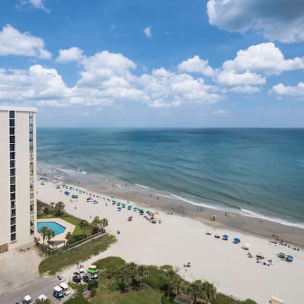A beachfront hotel with a pool, beach umbrellas, and a view of the ocean.