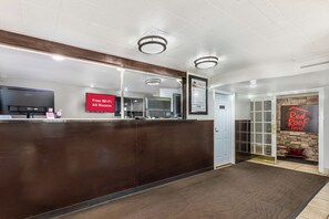 A hotel reception area with a dark reception desk, a 'Free Wi-Fi All Rooms' sign, a 'Red Roof Inn' sign, and a modern interior design. - Red Roof Inn North Dallas - Park Central (Dallas)