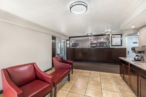A reception area with a counter, two red chairs, a coffee machine, and a framed menu on the wall. - Red Roof Inn North Dallas - Park Central (Dallas)