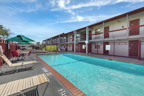 Une piscine dotée de chaises longues et d’un espace abrité, le tout entouré d’un immeuble à plusieurs étages avec des balcons.