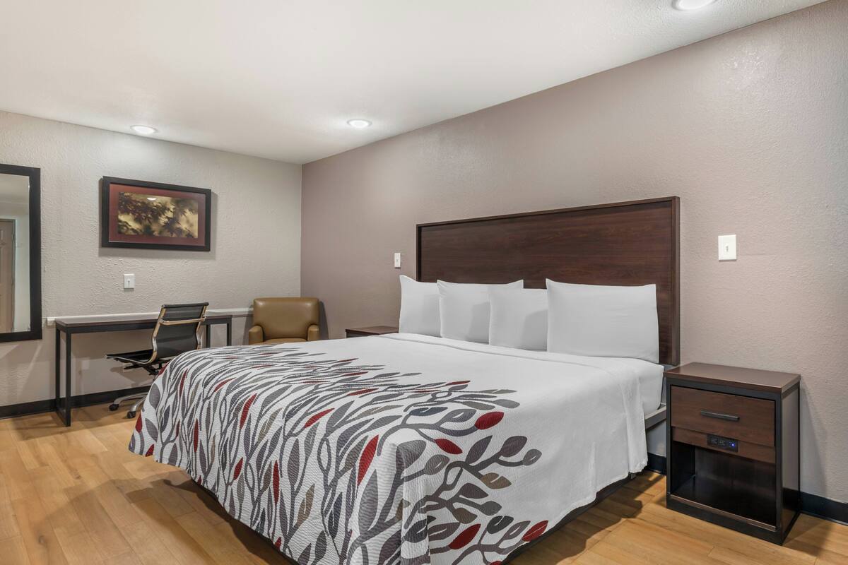 A hotel room with a bed, desk, chair, and nightstand.
