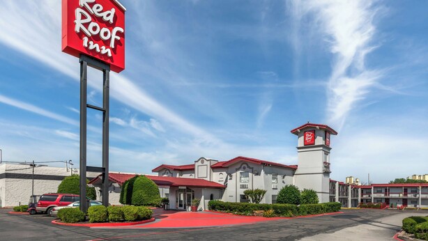 Ein Red Roof Inn mit einem auffälligen roten Schild, einem Parkplatz und einem Gebäude mit rotem Dach.