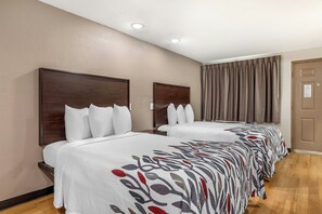 Une chambre d’hôtel avec deux lits, une tête de lit en bois, une grande fenêtre avec des rideaux et une porte avec une pancarte.