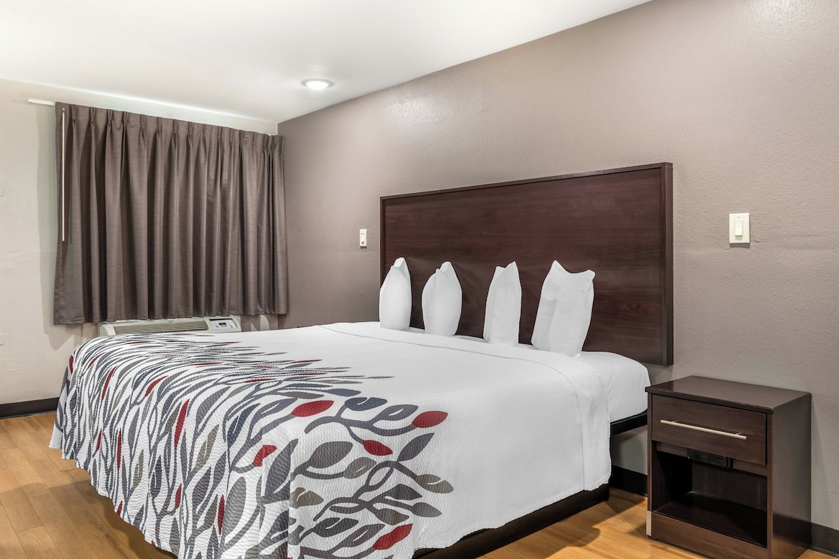 A hotel room with a large bed, a bedside table, and a window with curtains.