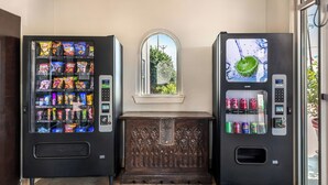 Two vending machines with snacks and drinks, a window with a view, and a decorative wooden bench. - Red Roof Inn North Dallas - Park Central (Dallas)