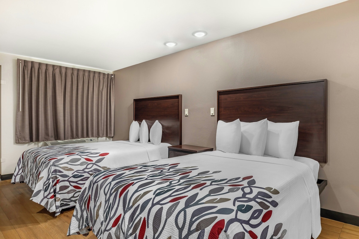 A hotel room with two beds, a large window with curtains, and a wooden headboard.