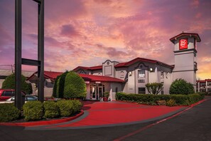 A hotel with a red roof, a tower with signage, and a red carpeted entrance. - Red Roof Inn North Dallas - Park Central (Dallas)