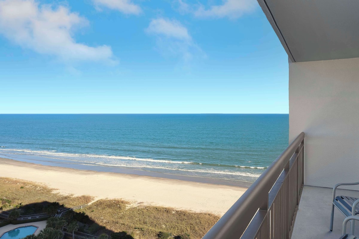 A balcony with a view of the beach and ocean.