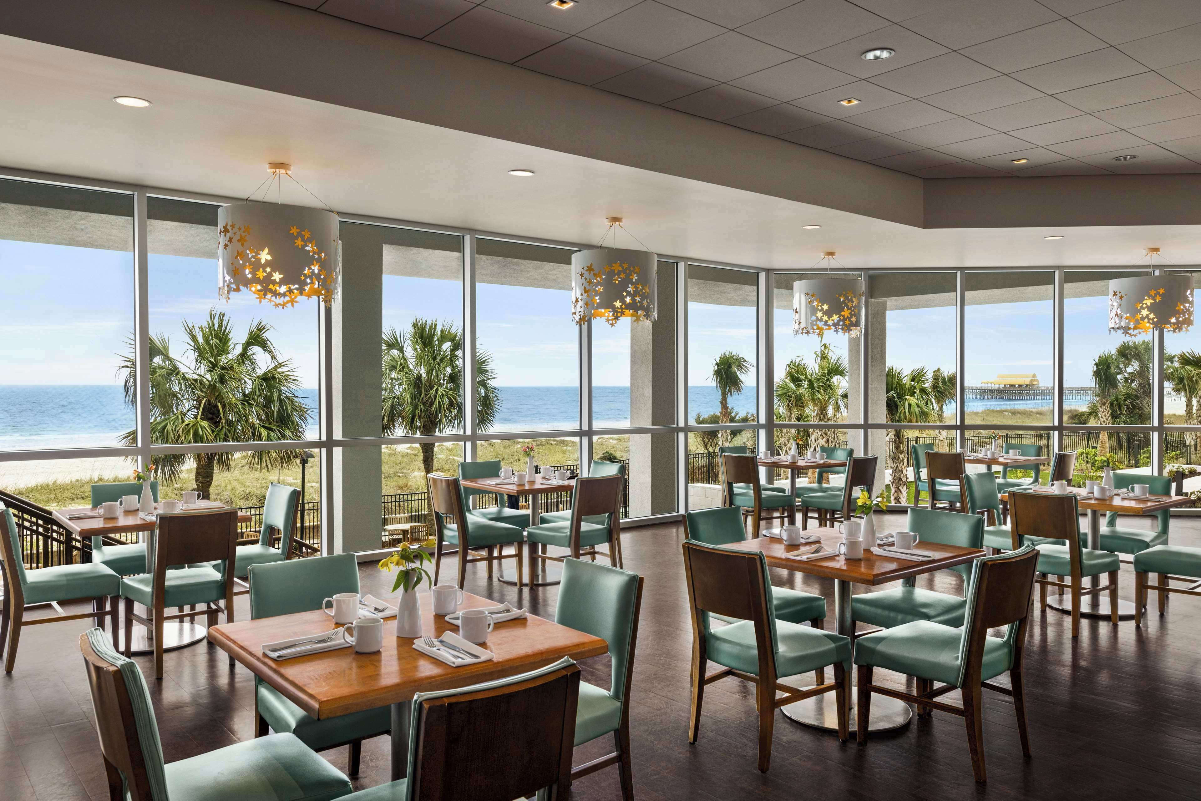 A restaurant with tables and chairs, large windows, and a view of the ocean.