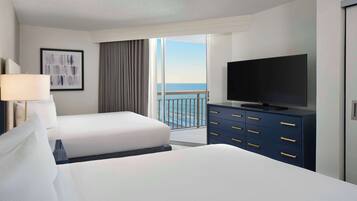 A hotel room with a large bed, a TV on a dresser, and a balcony with a view of the ocean.