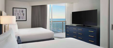 Habitación de hotel con una cama grande, un televisor en una cómoda y un balcón con vista al océano.