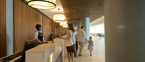 Et hotellets reception område med moderne design, med en receptionsdisk, store hængende lamper, og en rummelig lobby med højt til loftet og søjler.
