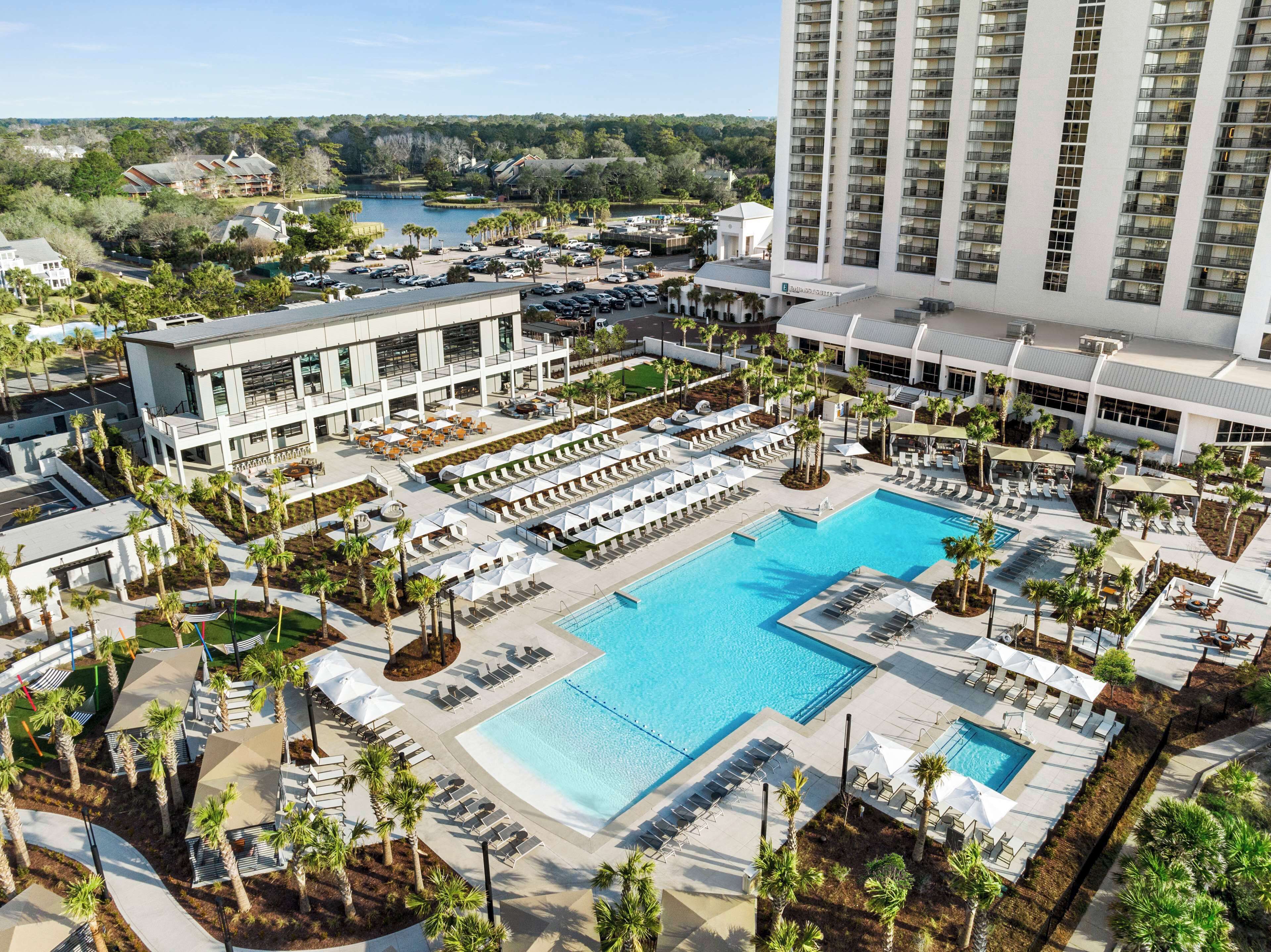 A hotel with a large pool area, multiple lounge chairs, and a view of a lake.
