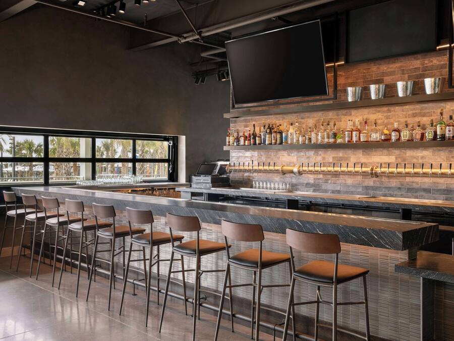 A modern bar area with a long counter, multiple stools, and a variety of liquor bottles.