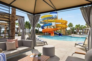 A pool area with a water slide, lounge chairs, and a covered seating area. - Embassy Suites by Hilton Myrtle Beach Oceanfront Resort (Myrtle Beach)