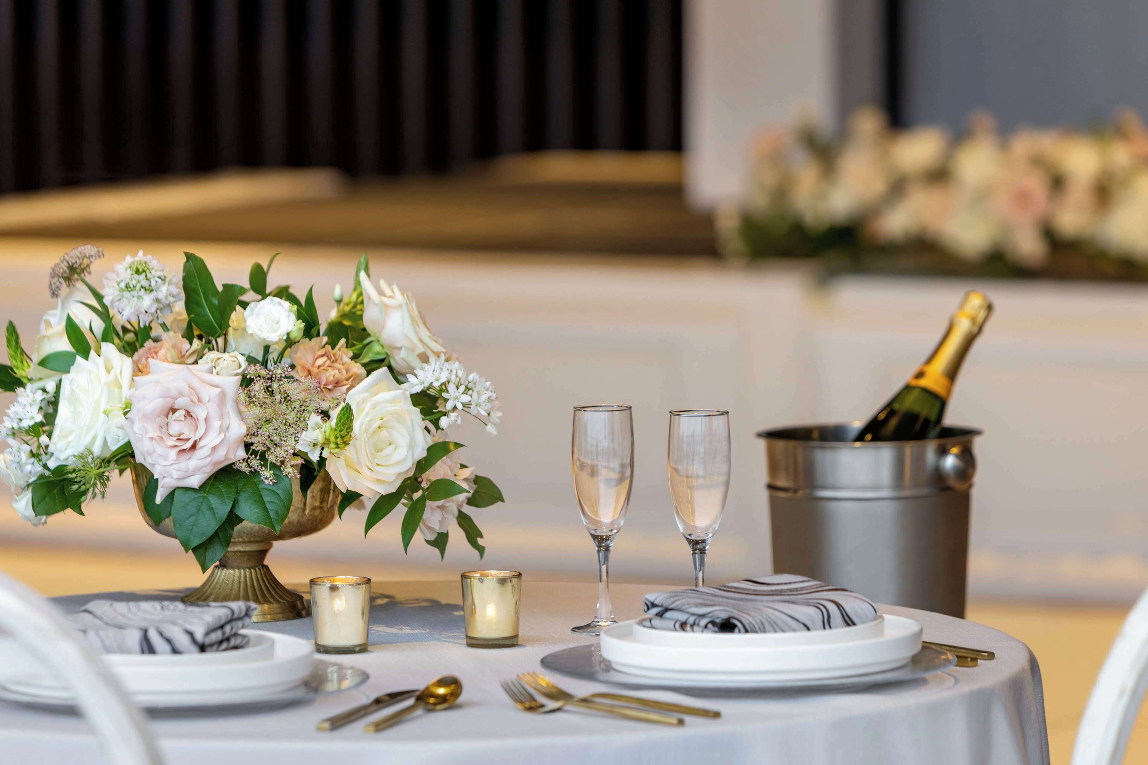 A table set for a formal event with a floral centerpiece, champagne glasses, and a bottle of champagne in a bucket.