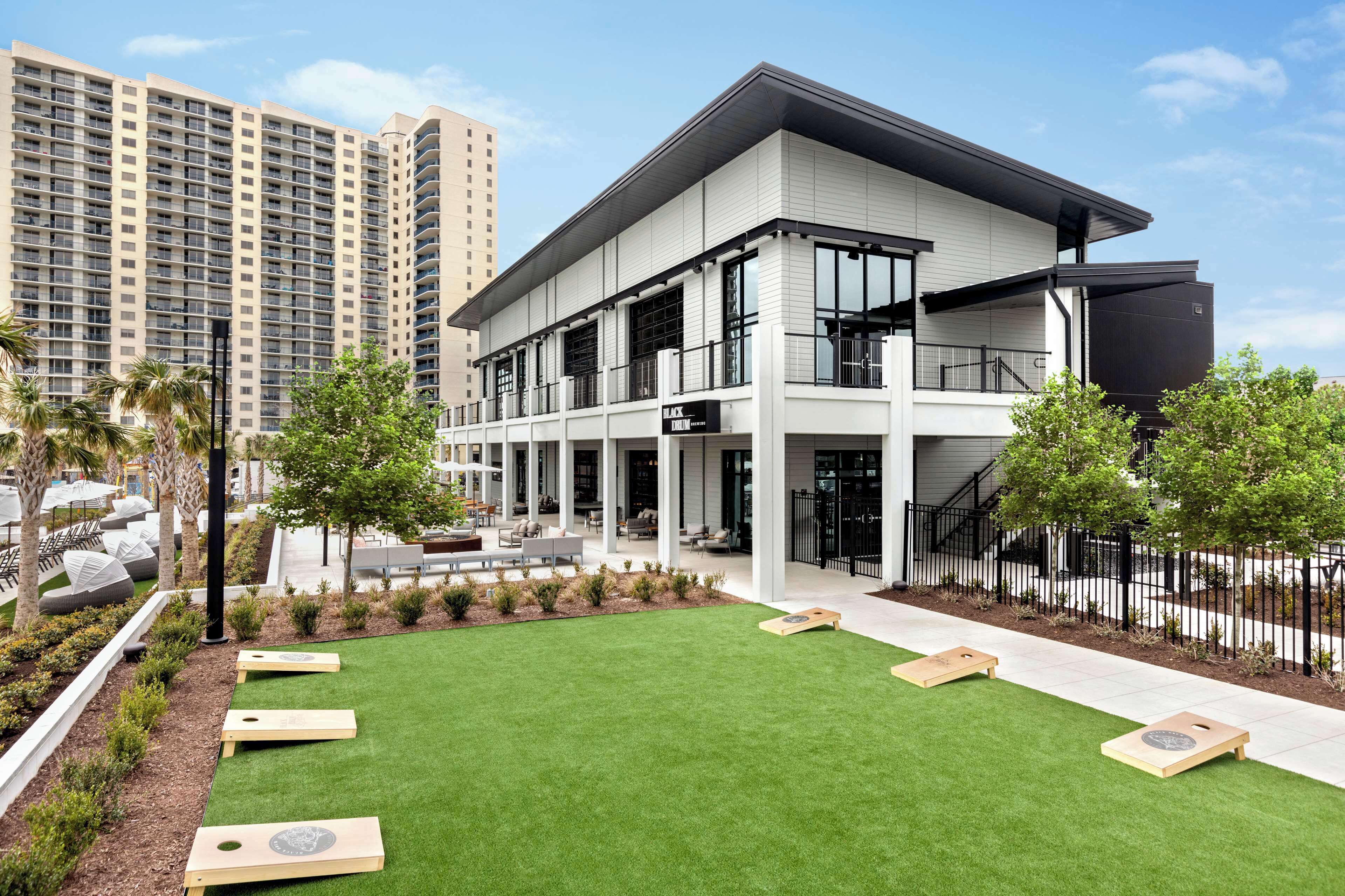 A modern building with a flat roof, large windows, and a courtyard with artificial grass and wooden planters.