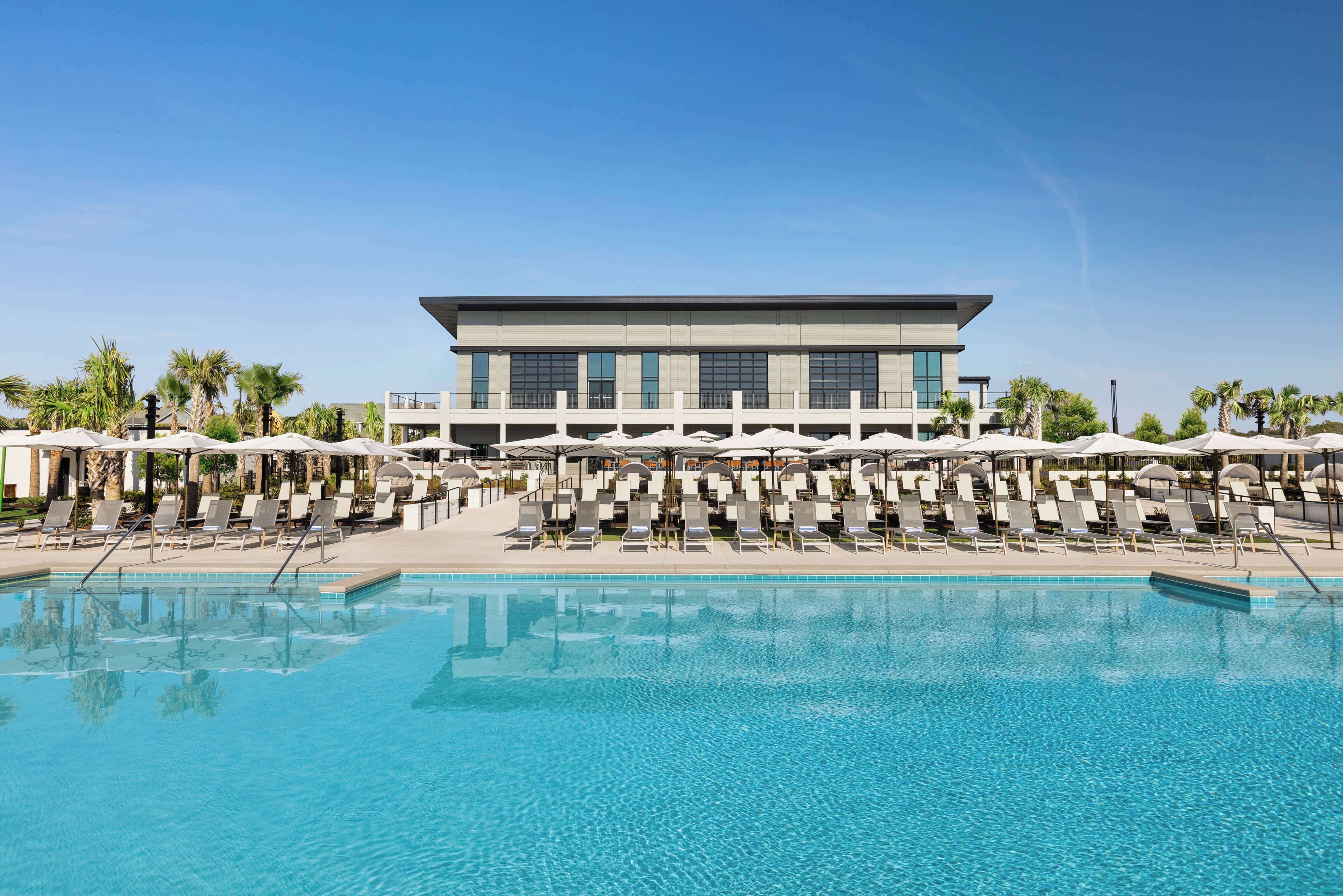 A modern hotel with a large pool, sun loungers, and umbrellas.