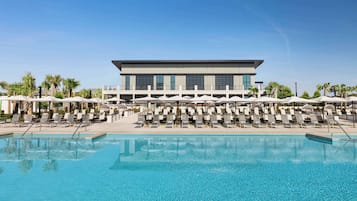 A modern hotel with a large pool, sun loungers, and umbrellas.