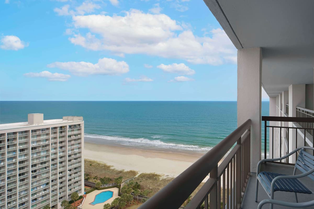 A high-rise hotel with a balcony overlooking a beach and ocean.