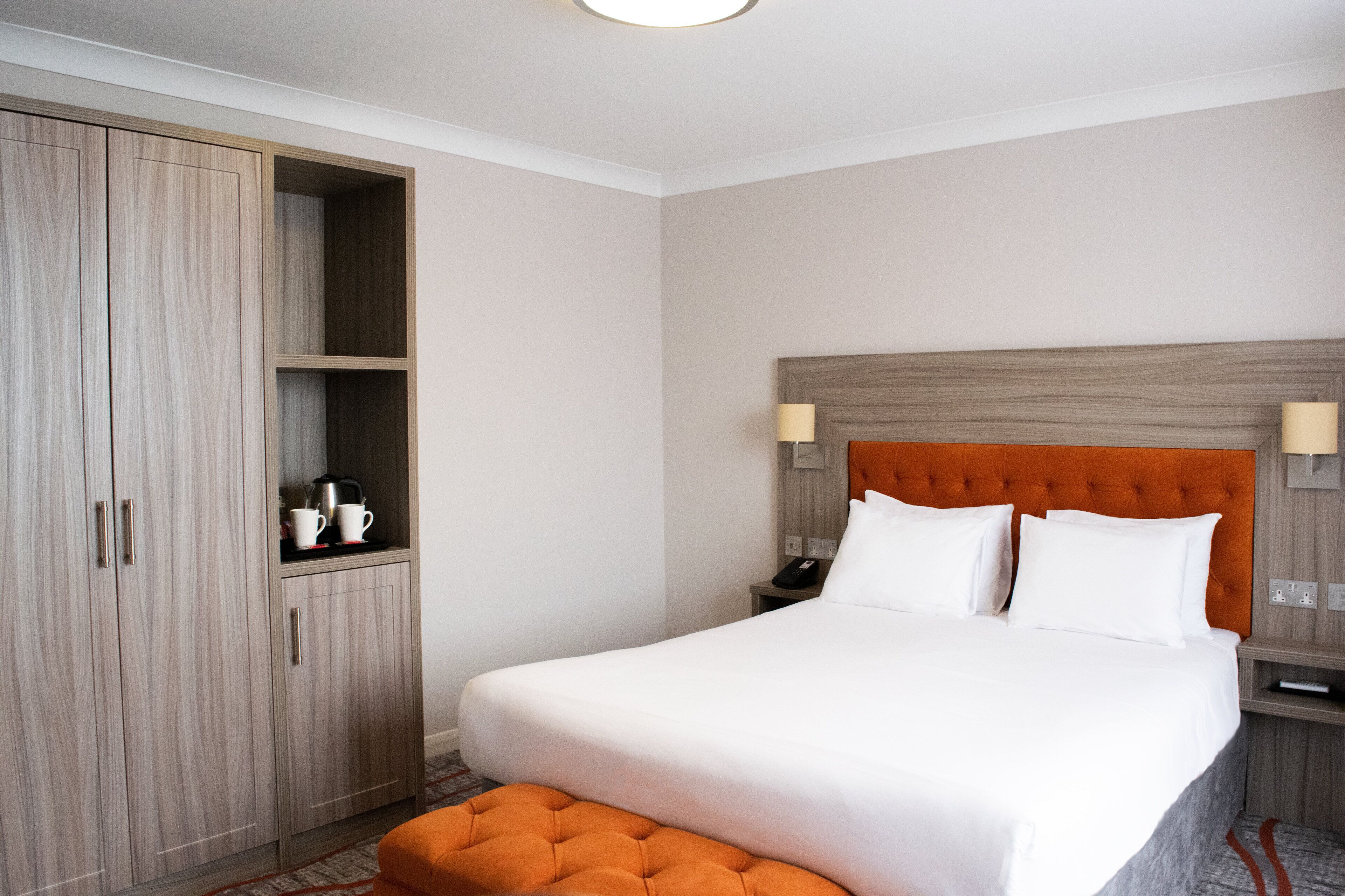 A hotel room with a large bed, a wardrobe, and a nightstand with a lamp.