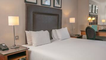 A hotel room with a large bed, two bedside lamps, a desk with a phone, and a mirror above the desk.