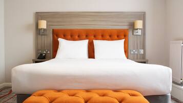 A large bed with a tufted headboard, two bedside lamps, a telephone, and a radiator.