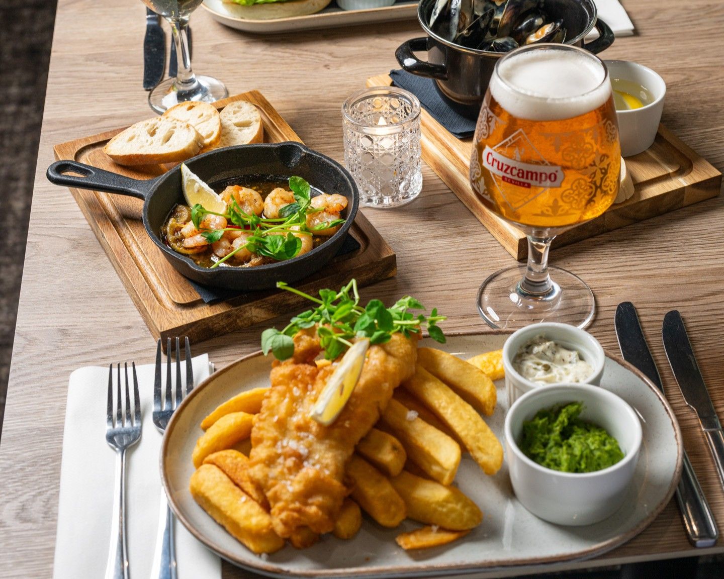 Un plato de pescado con papas fritas, una cerveza en vaso y un bol de salsa.