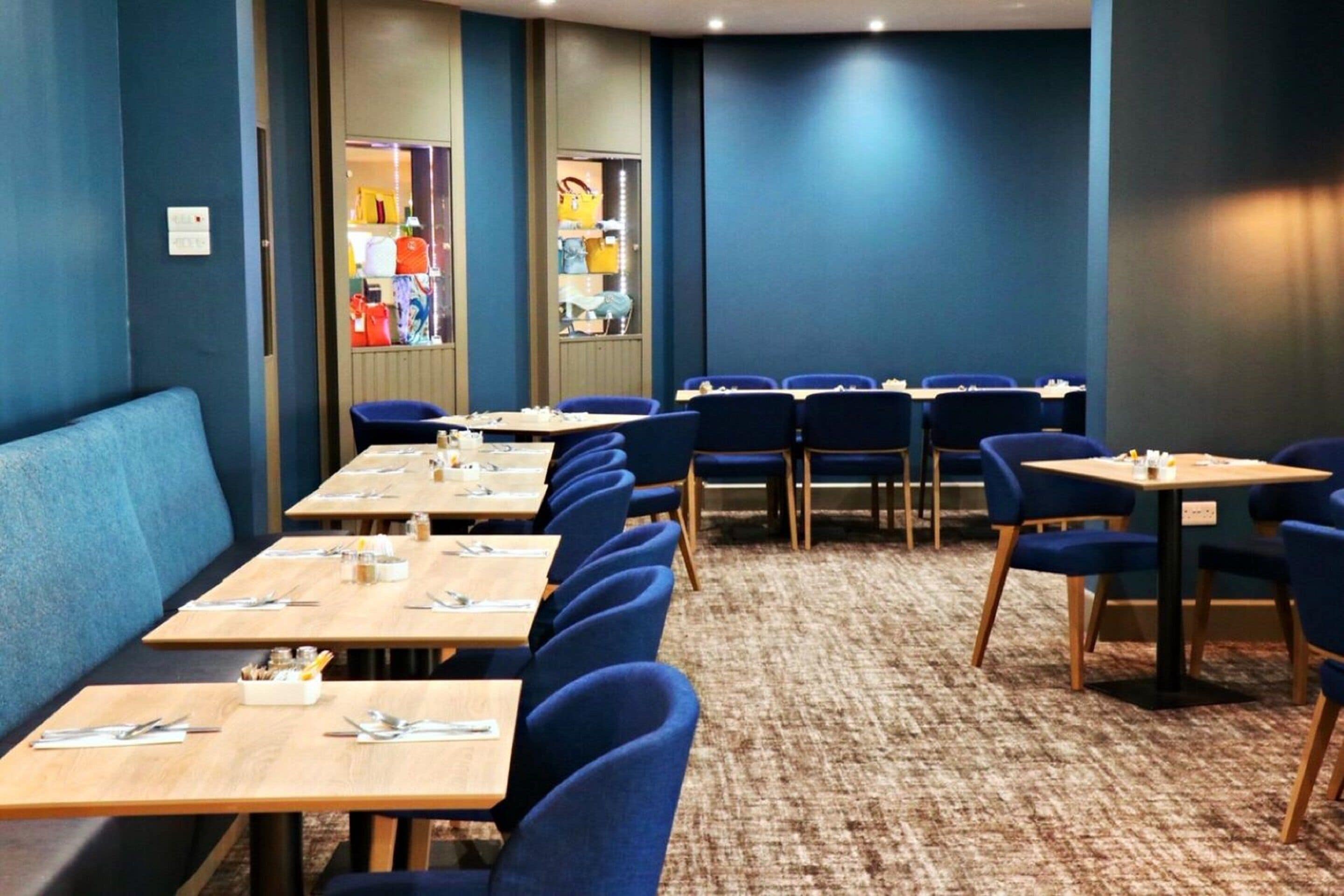 Une salle à manger d’hôtel avec plusieurs tables et chaises, un sol recouvert de moquette et un mur bleu.